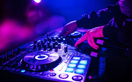 DJ console mixing music hands and with blurred people dancing night club party DJ console mixing music hands and with blurred people dancing night club party